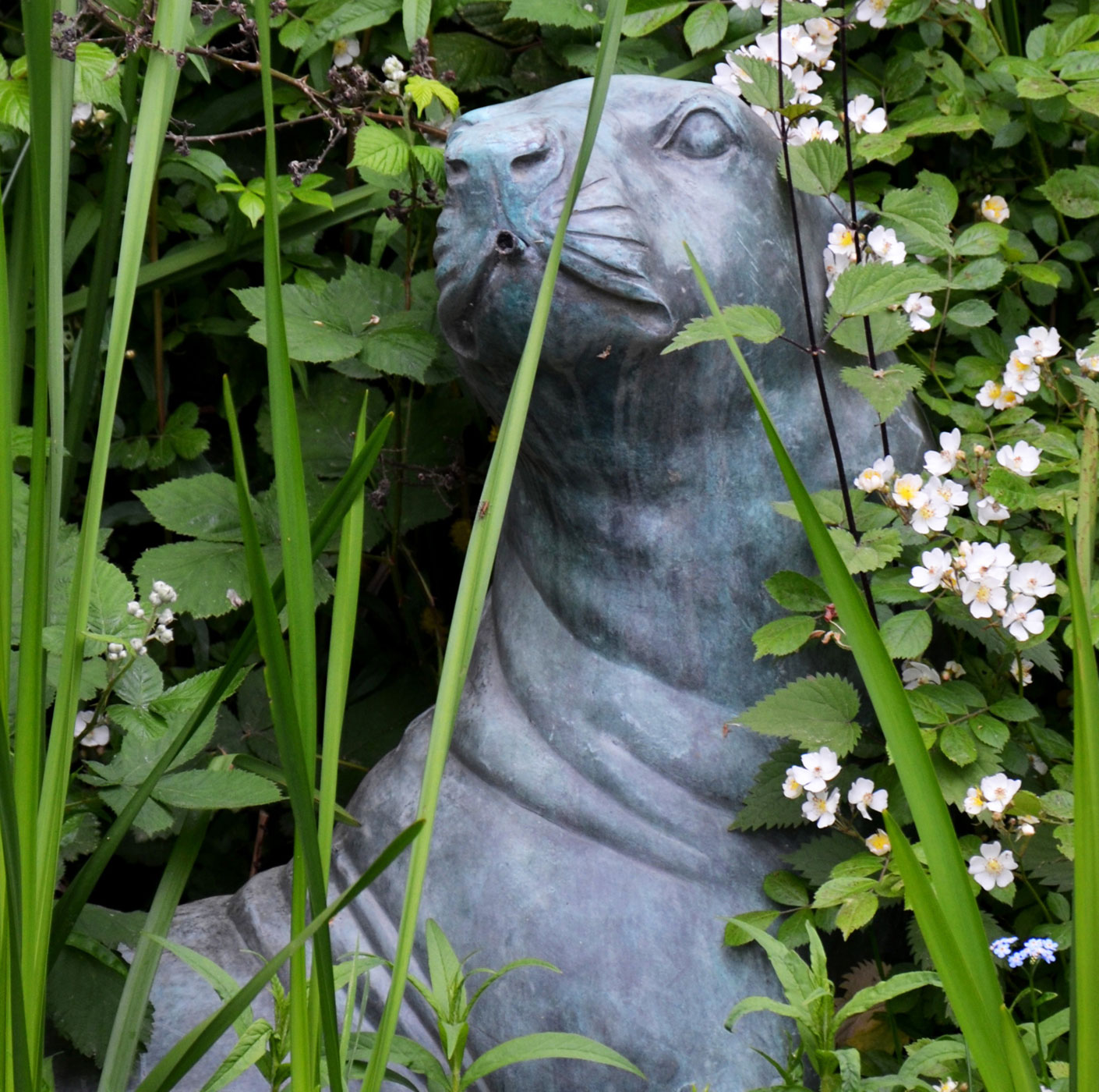 Eine Skulptur in Form einer Robbe zwischen Gräsern und Blumen als Beispiel für Kunst im Garten.