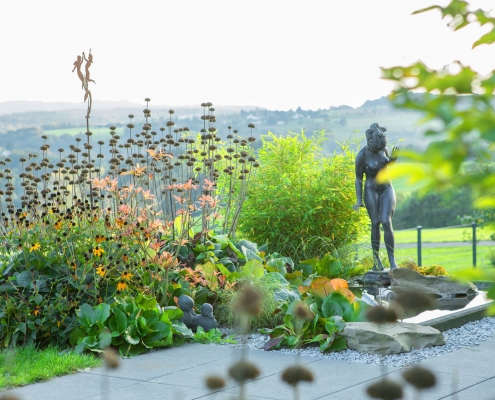Ausgefallene Blütenstände der Phlomi mit Bronzestatue einer nackten Frau in einem Garten in der Landschaft.
