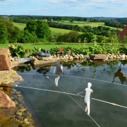 Gartenkunst Drahtseilakt über dem Gartenteich mit schönem Blick in die hügelige Landschaft bei Eitorf