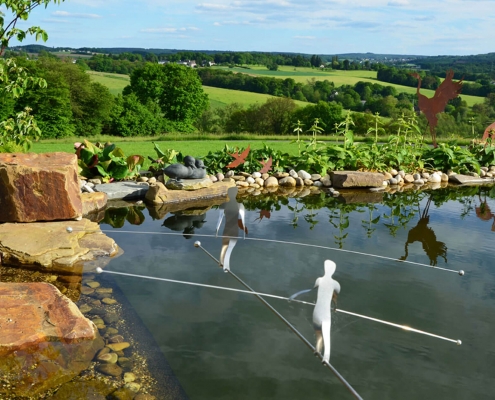 Gartenkunst Drahtseilakt über dem Gartenteich mit schönem Blick in die hügelige Landschaft bei Eitorf
