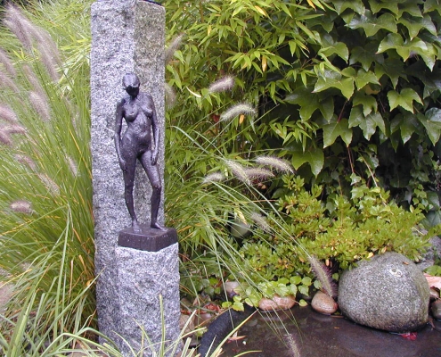 Steinstelen auf denen eine Bronzestatue einer nackten Frau steht als Beispiel für Kunst im Garten.