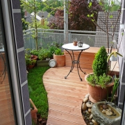Gartengestaltung eines Balkon mit kleiner Rasenfläche, Bankirai Terrasse und Pflanzkübel.