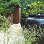 Stelen aus rostigen Stahl und grüne Büsche, Gartenkunst Vasenbrunnen im Kiesgarten mit Bonsai Kiefern.