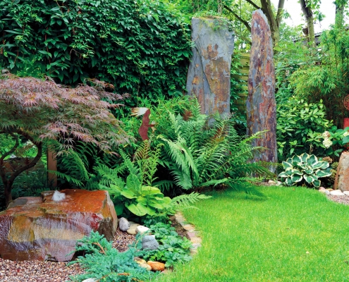 Mannshohe Schieferstelen, Farn, Büschen und Rasen in einem modernen Garten.