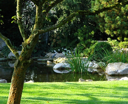 Pagode aus Stein in einem japanischen Garten vor einer Wiese mit Gartenteich, angelegt durch Manfred Wilczek in Hennef.