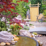 Steinbrücke mit Blick auf eine Sitzecke in einem japanischen Garten.
