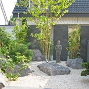 Meditationsecke mit Buddhafigur, die auf Kies steht im Garten vor einem weißen Haus.