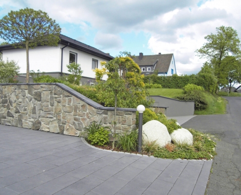 Steinmauer an einem Einfamilienhaus zur Abgrenzung der Parkfläche aus Naturstein und ein Blumenrabatt.
