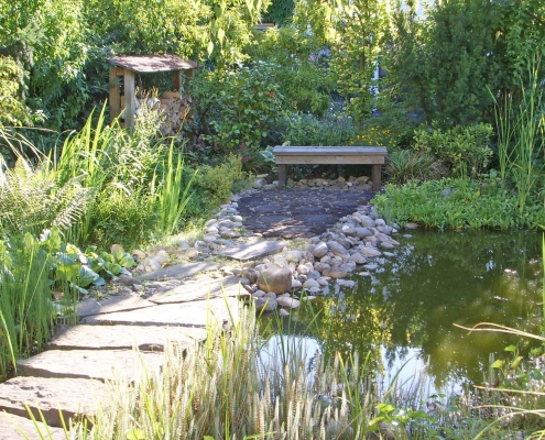 Teich Biotop und alter Baumbestand in einem Garten mit einer Holzbank.