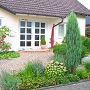 Natursteinpflaster im Eingangsbereich eines Hauses mit einem natürlich wirkenden Garten.
