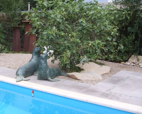 Seehundskulptur aus Bronze sitzen in einem Kiesbett am Pool