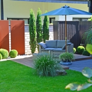 Loungemöbel auf einer Gartenterrasse mit Sichtschutz aus Koniferen, Holzelementen und rostigen Stahl.