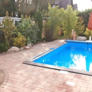Schwimmbad im Garten mit Pflastersteinen und grüner Umrandung