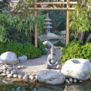 Tiefenwirkung durch einen Spiegel, der an einem Bambusgestell aufgehängt ist, im japanischen Garten mit Steinen und einer Buddhafigur.