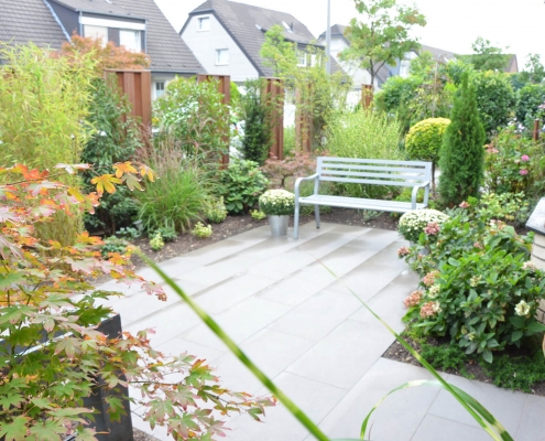 Vorgarten mit grauen Gehwegplatten und einem Sichtschutz auf Bankirai, Gräsern und Formgehölzen sowie wie einem blauen Bank geplant durch Wilczek Gartenbau.