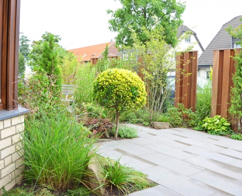 Vorgarten mit grauen Gehwegplatten und einem Sichtschutz auf Bankirai, Gräsern und Formgehölzen geplant durch Wilczek Gartenbau.