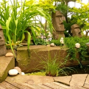 Wasserbecken mit grünen Pflanzen und Osterinsel Figuren auf einem Balkon.