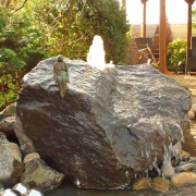 Basaltfindling mit kleinen Springbrunnen und einer Bronzefigur in Form einer sitzen Frau von Gartenbau und Gartengestaltung Wilczek in Hennef.