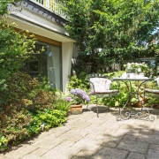 Garten im English Cottage Stil mit filigranem Eisentisch und Eisenstühlen.