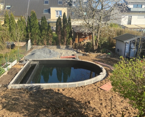 Die Gartenbaustelle von einem Schwimmteich, in den schon Wasser gefüllt ist, vor der Fertigstellung.